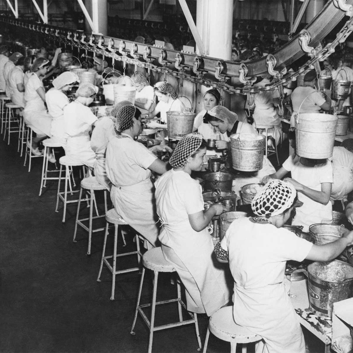 A black and white photo of women with hair-nets working on a factory assembly line.