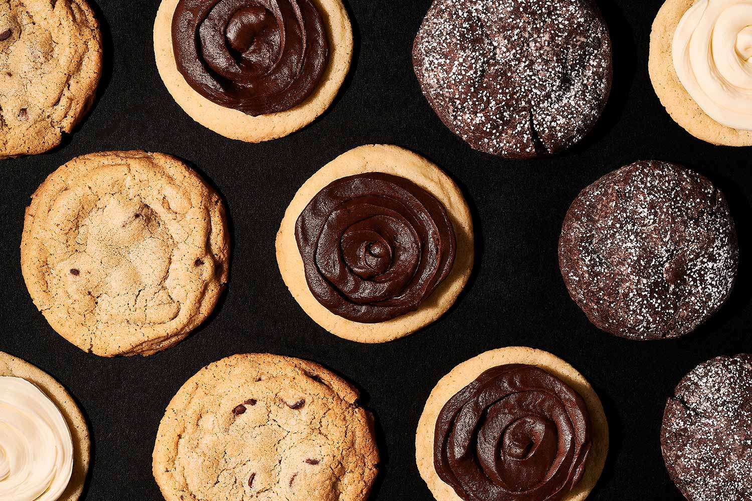 Eleven different cookies with various toppings on a black background.