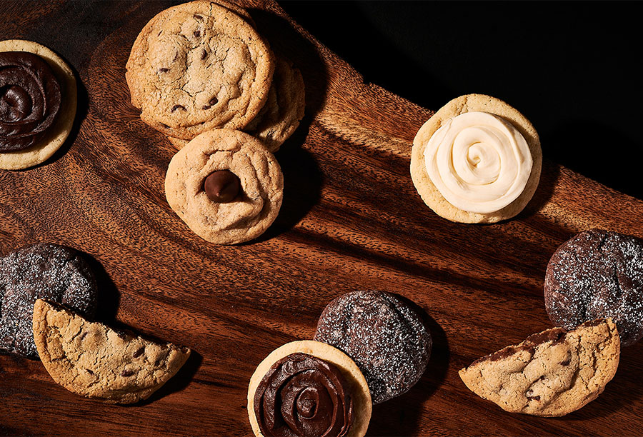 Ten assorted cookies on a dark wooden table, some cut in half.