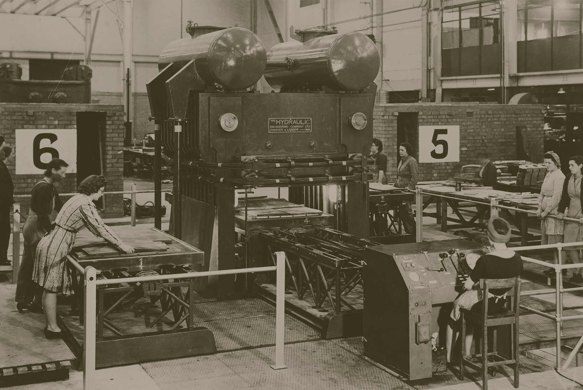 A sepia-colored image of seven women working in a factory machinery room.